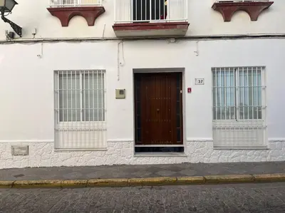 a white building with a brown door and three windows at Apartamento Veracruz in Rota