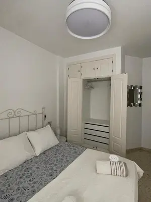 a white bedroom with a bed and a white lamp at Puerta de Doñana: Playa y centro a un paso. in Sanlúcar de Barrameda