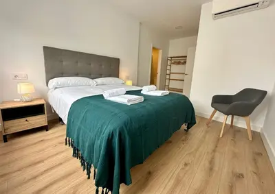 a bedroom with a bed with a green blanket and a chair at Apartamentos La Muralla Grupo AC Gestion in Cádiz