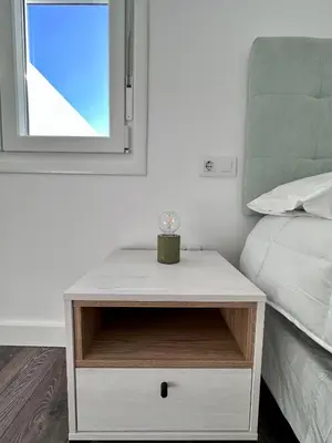 a white nightstand next to a bed with a window at Apartamentos La Muralla Grupo AC Gestion in Cádiz