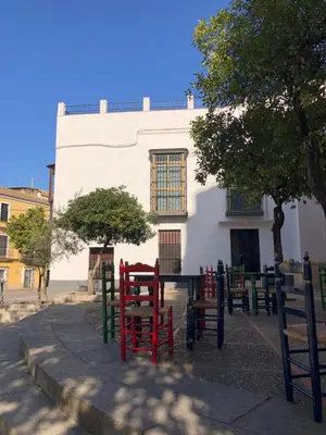 a white building with red and green chairs in front of it at Apartamentos Makao Puerta del Olivillo in Jerez de la Frontera