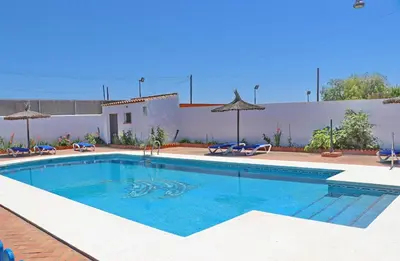 a swimming pool in a yard with chairs and umbrellas at Chalet Florida III in Conil de la Frontera