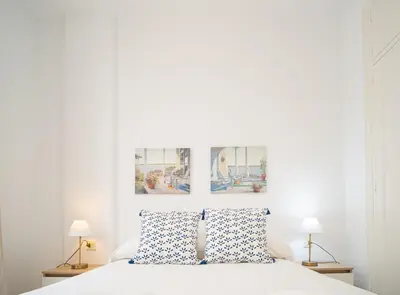 a white bedroom with a bed with blue and white pillows at Sibs Sanlucar-San Juan-Cabildo Centro Playa Familias Amigos in Sanlúcar de Barrameda