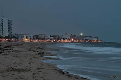 a beach at night with a city in the background at Hotel Macavi Playa in Rota