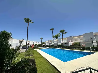 a swimming pool with palm trees in front of a building at Villa Bosque Novo Sancti petri Grupo AC Gestión in Chiclana de la Frontera