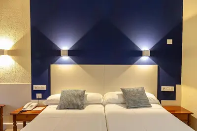 a bedroom with two beds with blue walls and lights at Hotel Caribe in Rota