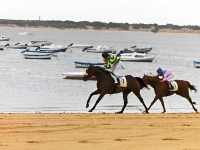 two people riding horses on the beach near the water at Apartamento Poniente Sanlúcar - Centro in Sanlúcar de Barrameda