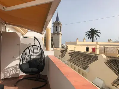 a chair sitting on a balcony with a clock tower at Apartamento DUPLEX CRUZ DEL MAR in Chipiona