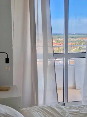 a bedroom with a bed and a window with white curtains at Frente al mar, preciosas vistas, piscinas , valdelagrana in El Puerto de Santa María