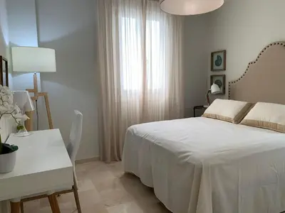 a white bedroom with a bed and a table and a desk at Coral Oro en la Caleta Ha Apartment in Cádiz