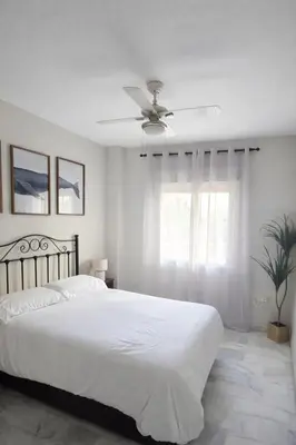 a white bedroom with a bed and a ceiling fan at La Alcazaba de Cristina in El Puerto de Santa María