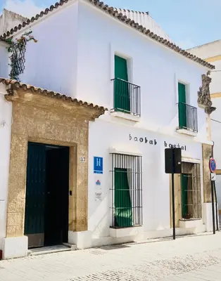 a white building with green doors on a street at Hostal Baobab in El Puerto de Santa María