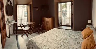 a bedroom with a bed and a table and two windows at Hostal Baobab in El Puerto de Santa María