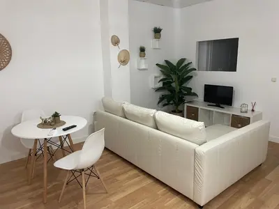 a white living room with a white couch and a table at Acogedor apartamento. in Sanlúcar de Barrameda