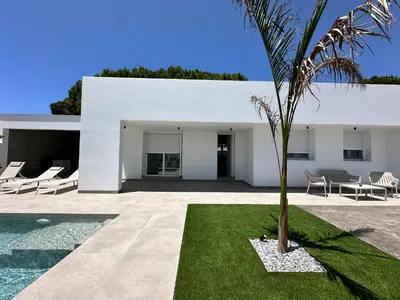 a white house with a palm tree in the yard at Alda & Aljosía in Chiclana de la Frontera