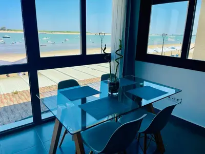 a glass table with chairs and a view of the beach at Duplex ático Bajo de Guía in Sanlúcar de Barrameda