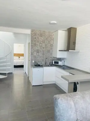 a kitchen with white cabinets and a living room at Duplex ático Bajo de Guía in Sanlúcar de Barrameda