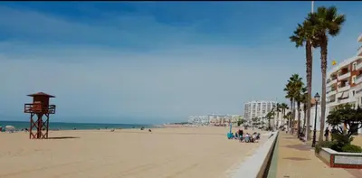 a beach with palm trees and buildings and people on it at Villa Zeus in Rota
