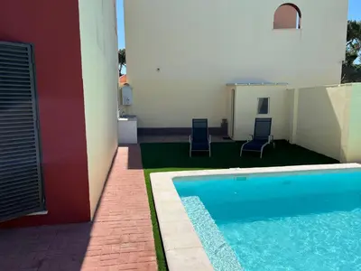 a swimming pool next to a building with two chairs at Casa piscina Playa Barrosa Delfin 6 in Chiclana de la Frontera