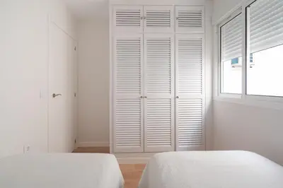 a white bedroom with two beds and a window at Apartoyou - Plaza de Toros in El Puerto de Santa María