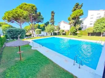 a swimming pool with an umbrella next to a building at Apartamento en Puerto de Santa María, Playa Las Redes in El Puerto de Santa María