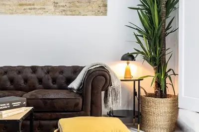 a living room with a brown couch and a plant at La Casa del Mercader by Gades Gestión in Cádiz