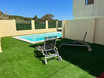two chairs sitting on the grass near a swimming pool at Casa piscina playa Barrosa Delfin 7 in Chiclana de la Frontera