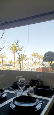 a table with plates and glasses and a window with palm trees at Playa Doñana 1 in Sanlúcar de Barrameda