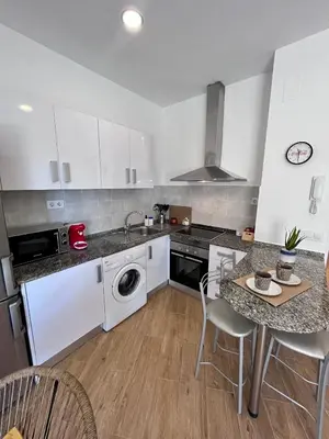 a kitchen with white cabinets and a table with chairs at GATU Villa Atardecer en la playa de las Redes 