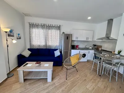 a living room with a blue couch and a kitchen at GATU Villa Atardecer en la playa de las Redes 