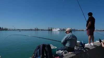 a man is sitting on a dock with a fish in the water at LA VICTORIA in Cádiz