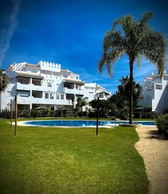 a large white building with a swimming pool and a palm tree at MyChoice Terraces in Rota
