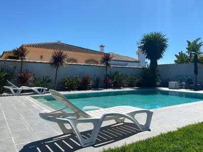 a swimming pool with two lounge chairs and a house at Villa Árbol del Tule in Chiclana de la Frontera