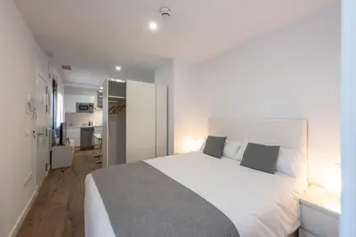 a bedroom with a large white bed and a kitchen at Apartamentos Santa María 15 in Jerez de la Frontera