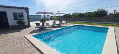 a swimming pool with chairs and umbrellas next to a house at Casa La Cabaña - Solo Familias in Chiclana de la Frontera