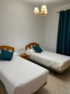 two beds in a room with blue curtains at VILLA LA MOMITA in Chiclana de la Frontera