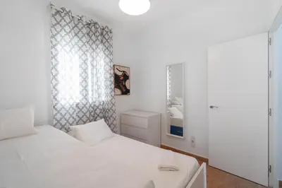 a white bedroom with a bed and a window at Apartoyou - Fuentebravía Playa in El Puerto de Santa María