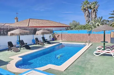 a pool with chairs and umbrellas next to a house at Chalet Blue in Conil de la Frontera