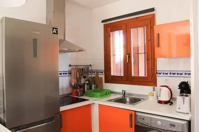 a kitchen with orange cabinets and a stainless steel refrigerator at Novo Sancti Petri, con piscina todo el año, La Mariposa by Chiclana Dreams in Chiclana de la Frontera