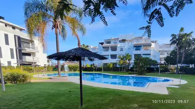 an umbrella in the grass next to a swimming pool at Rota Punta Candor Terrace Playa 3 Bajo C in Rota