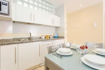 a kitchen with white cabinets and a table with wine glasses at Apartamento Playa Cádiz by ISA Hoteles in Cádiz
