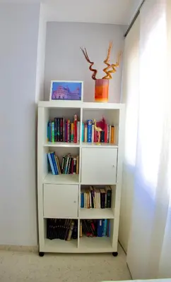 a white book shelf filled with books next to a window at El rinconcito de la Isla in San Fernando