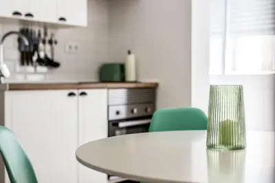 a white kitchen with a table and green chairs at Apartamento en CENTRO CIUDAD in El Puerto de Santa María